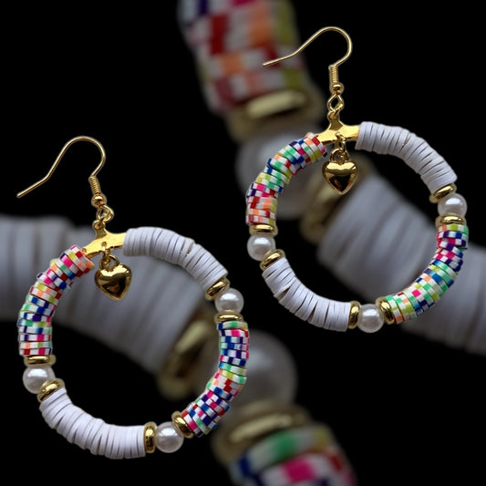 Handmade hoop earrings with white and rainbow clay beads, faux pearls, gold-tone accents, and a dangling gold heart charm, vibrant and playful statement jewellery on black background